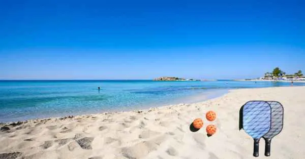 a beach with orange pickleballs with paddle on the beach sand