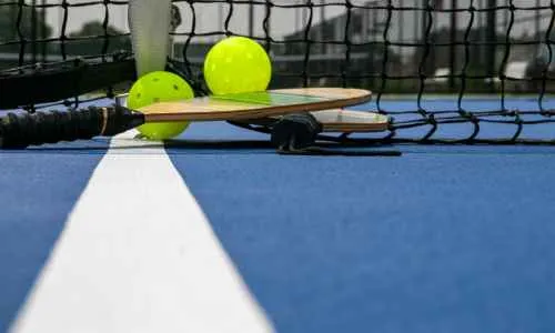 a pickleball paddle   and balls on a blue pickleball court surface
