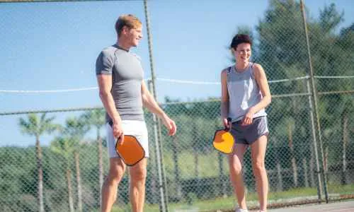 a person and women holding paddles on a pickleball court after completing a game.
