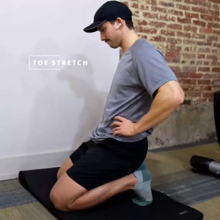 a person sitting on a mat and doing the Toe Stretch
